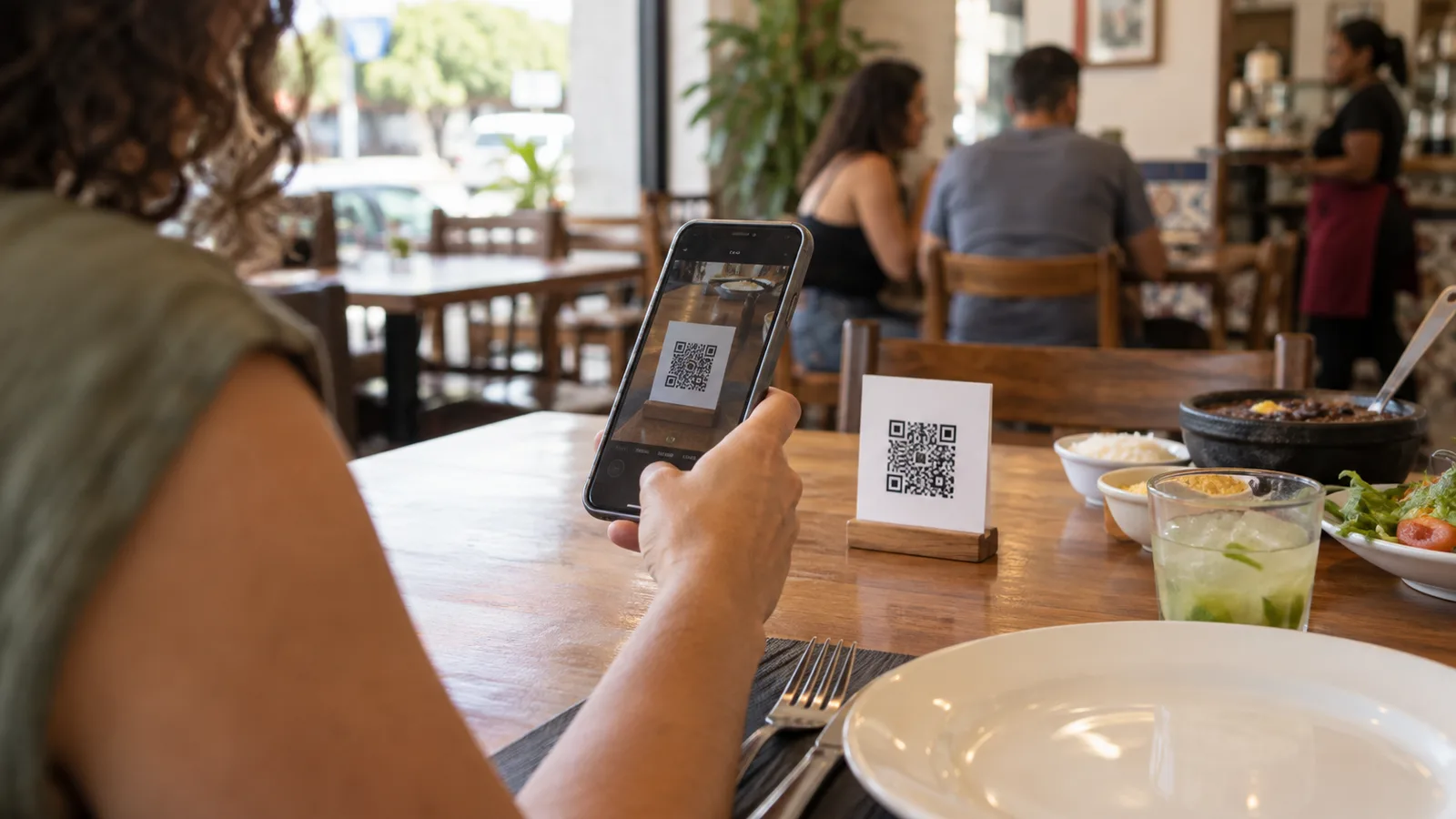 Cliente apontando o celular para um QR code sobre a mesa de um restaurante pequeno